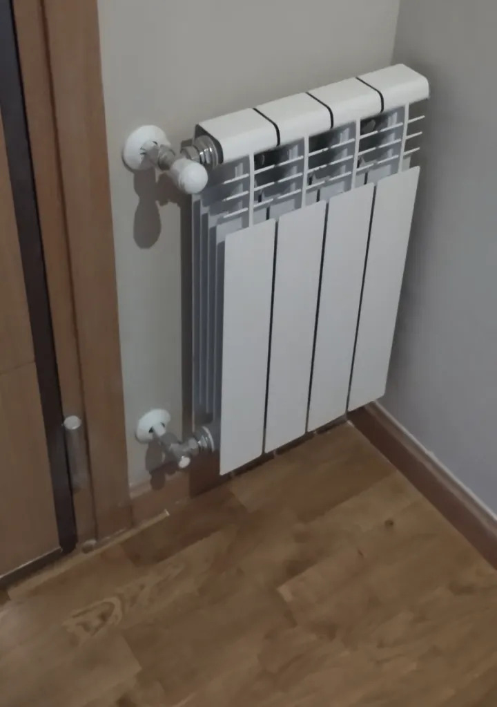 Radiador blanco junto a una puerta de madera sobre suelo de tarima