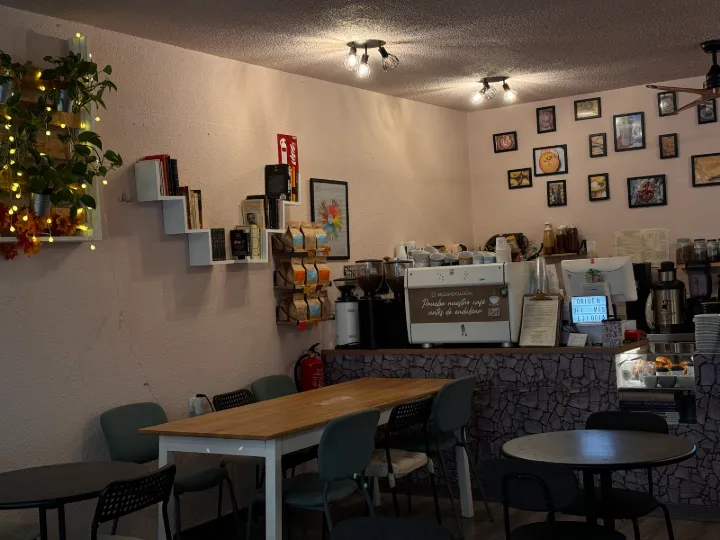 Interior de una cafetería con mesas, barra y estanterías en la pared